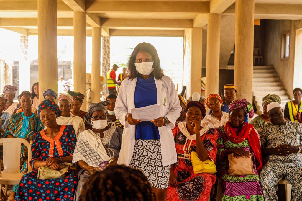 A masked healthcare professional standing among seated community members